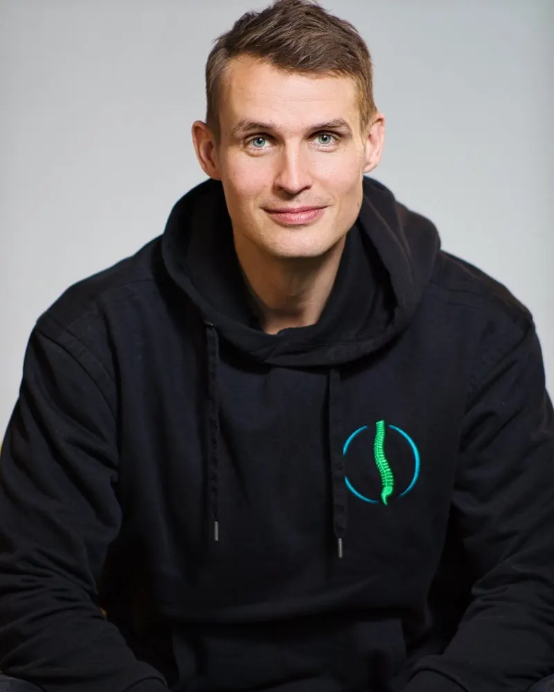 Portrait eines Mannes im schwarzen Hoodie mit Firmenlogo vor grauem Hintergrund